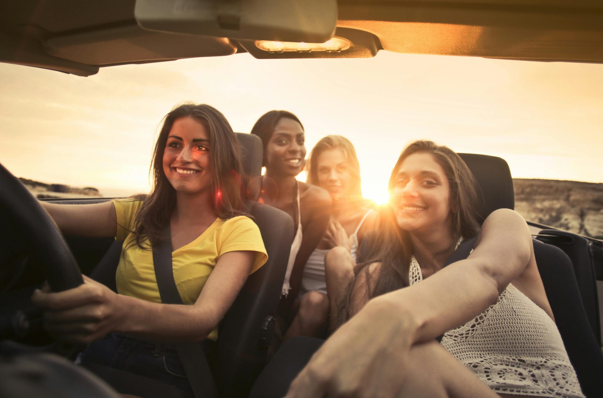 Four friends share smiles and laughter in a convertible during a sunset road trip in Malta.