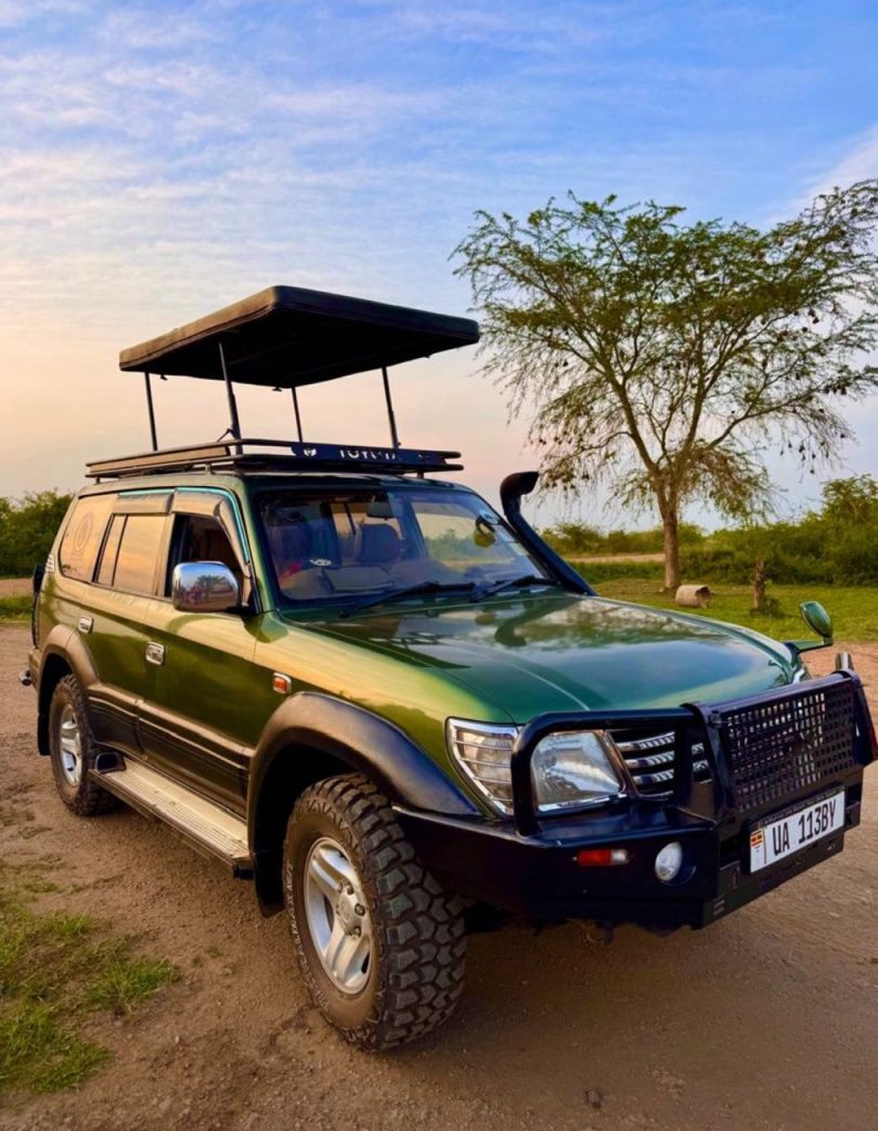 A 4x4 safari vehicle driving on a rugged dirt road with the misty mountains of Volcanoes National Park in the background, showing reliable car hire in Rwanda options